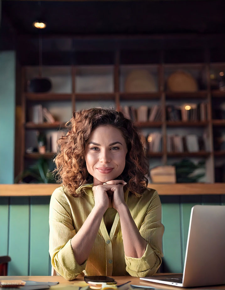Femme souriante dans un bureau chaleureux, symbolisant une praticienne ayant suivi une formation en hypnose spirituelle.
